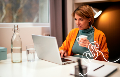 Mujer adulta tomando una taza de café mientras hace uso de un computador portatil